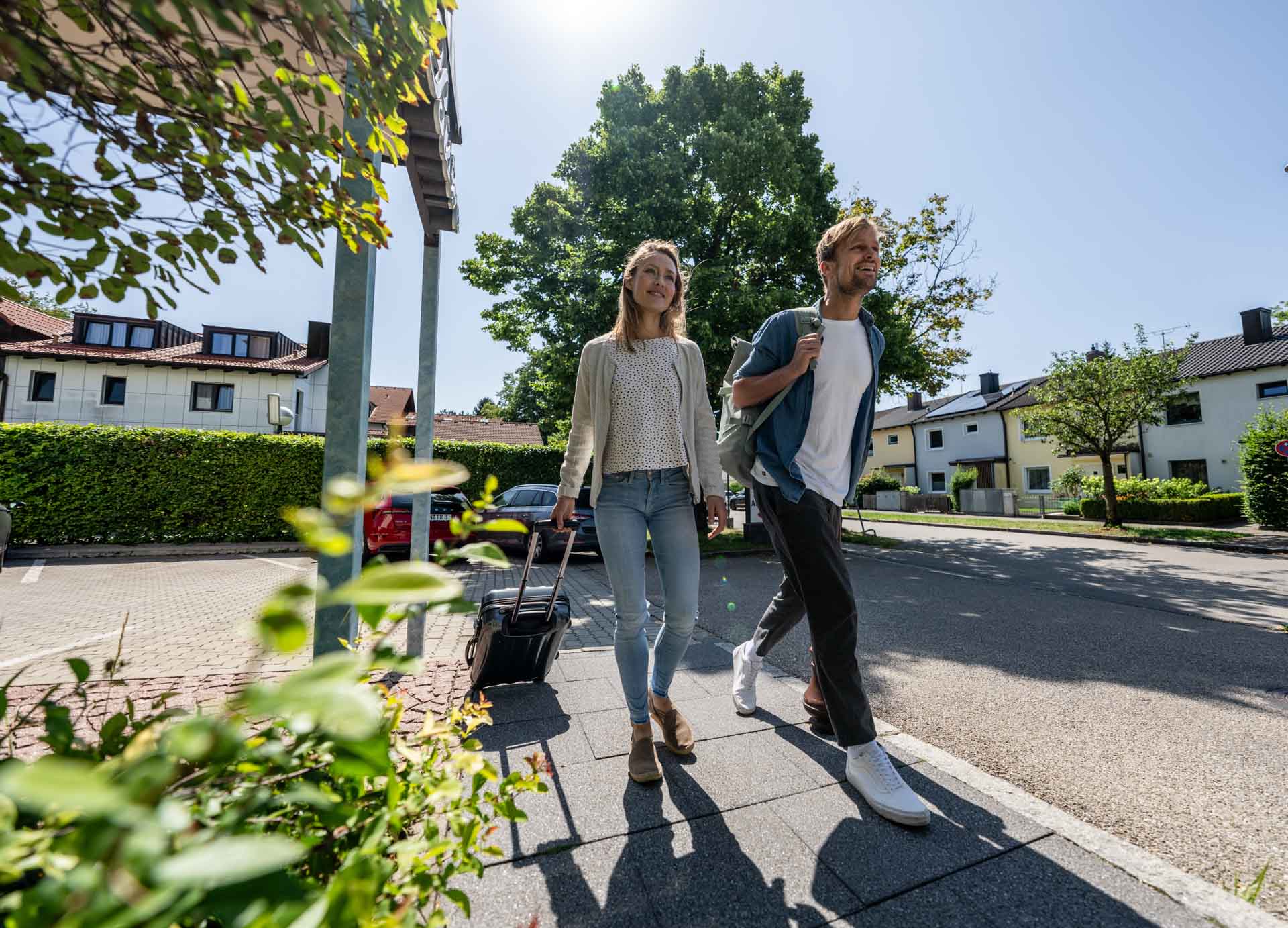 Weiblicher und männlicher Gast mit Koffer und Rucksack auf dem Weg in das Hotel am Moosfeld.